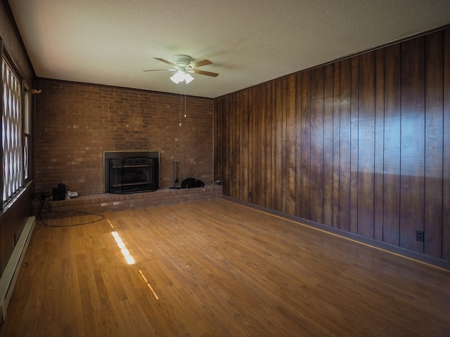 unfurnished living room featuring a brick fireplace, a baseboard radiator, a ceiling fan, a textured ceiling, and wood finished floors