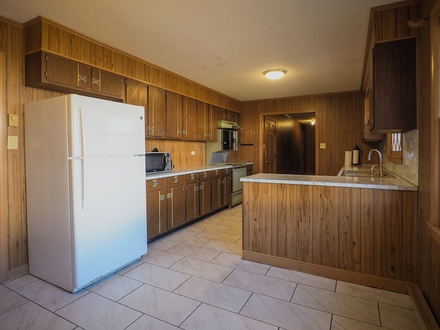 kitchen featuring range with electric stovetop, a sink, freestanding refrigerator, under cabinet range hood, and wooden walls