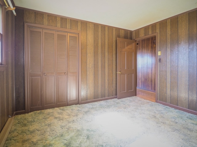unfurnished bedroom featuring baseboards, carpet flooring, a closet, and wooden walls