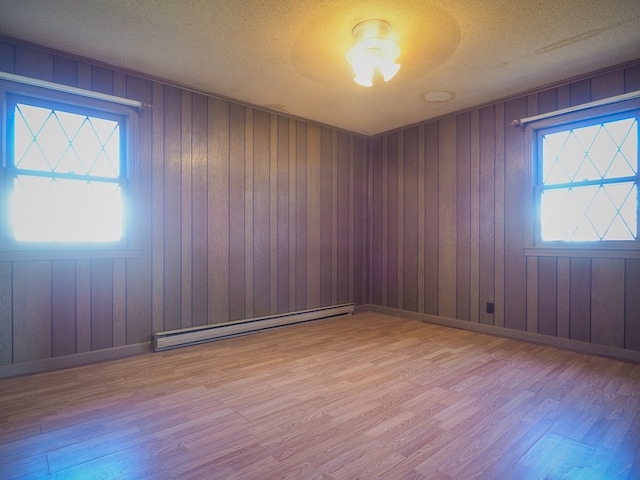 spare room featuring wooden walls, a baseboard heating unit, a textured ceiling, and wood finished floors