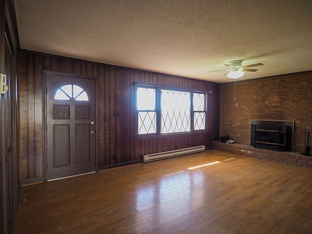 unfurnished living room featuring a wealth of natural light, a baseboard heating unit, a ceiling fan, and a textured ceiling