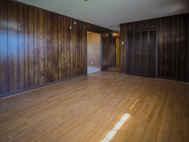 spare room with wooden walls, a textured ceiling, and wood finished floors