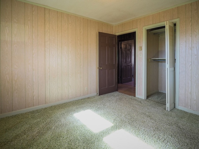 unfurnished bedroom featuring wood walls, carpet, a closet, and baseboards