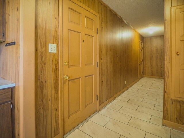 corridor with wood walls, a textured ceiling, and light tile patterned flooring
