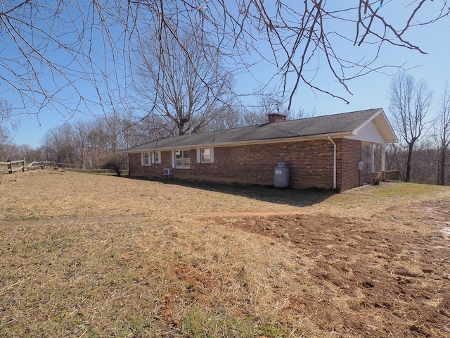 exterior space with brick siding, central AC unit, a lawn, and a chimney