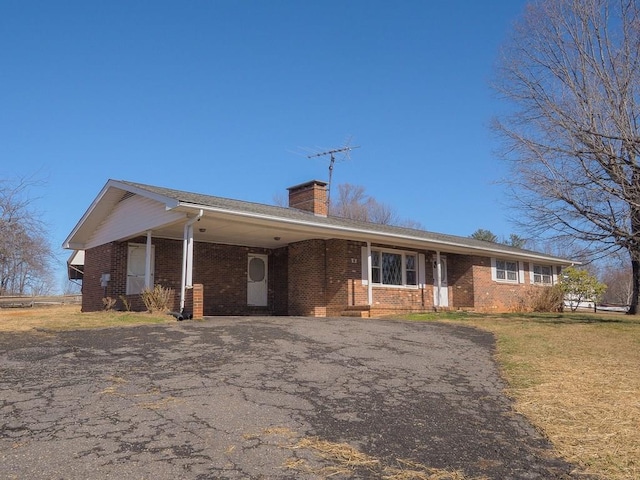 single story home featuring a front yard, brick siding, driveway, and a chimney