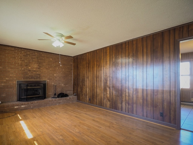 unfurnished living room with a fireplace, a textured ceiling, a ceiling fan, wood finished floors, and wood walls