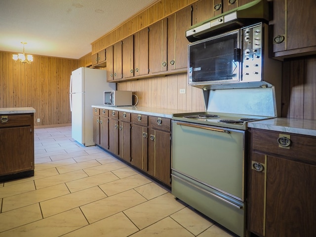 kitchen with stainless steel microwave, wooden walls, light countertops, freestanding refrigerator, and range with electric stovetop