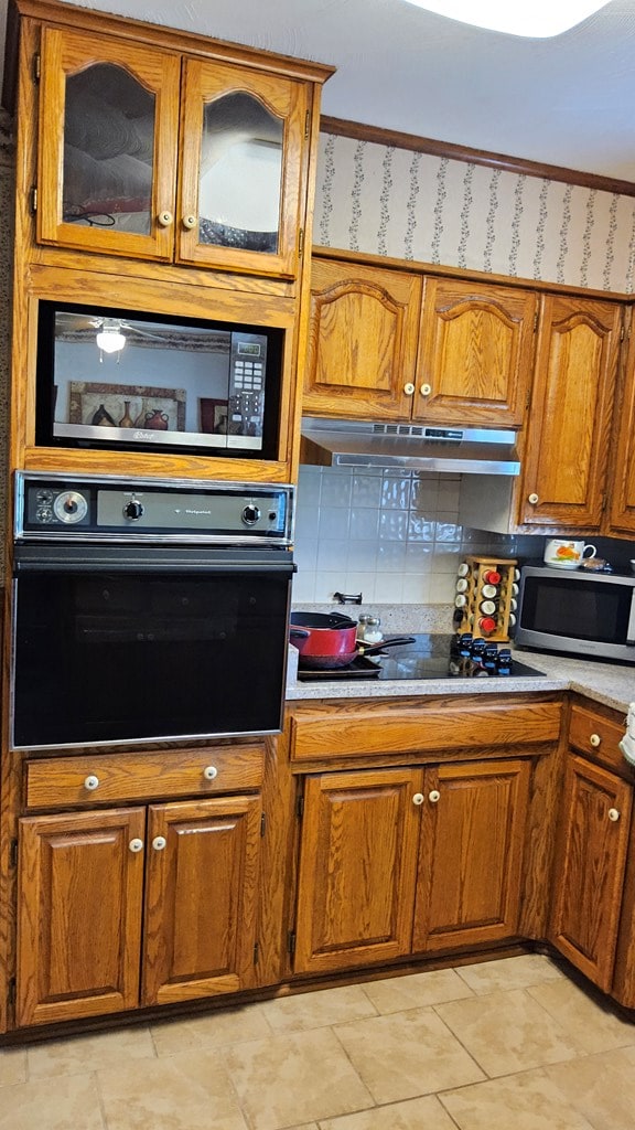 1359 Scratch Gravel Rd, Marion, VA 24354 - kitchen featuring black appliances, under cabinet range hood, brown cabinetry, glass insert cabinets, and light countertops