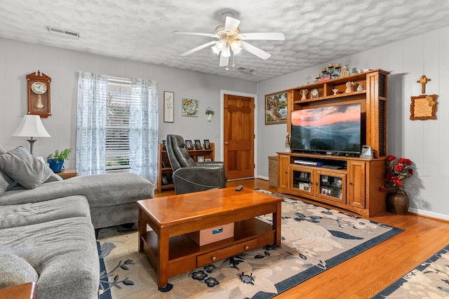 living room with ceiling fan, a textured ceiling, and light wood-type flooring