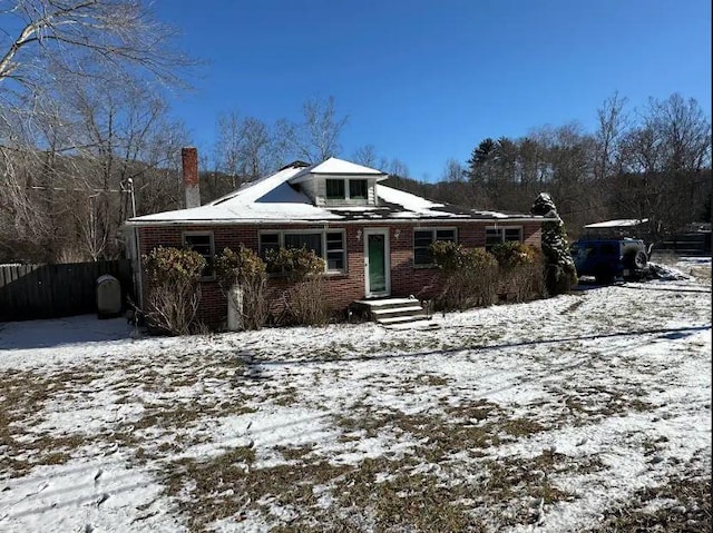 view of front of house with brick siding, a chimney, and fence