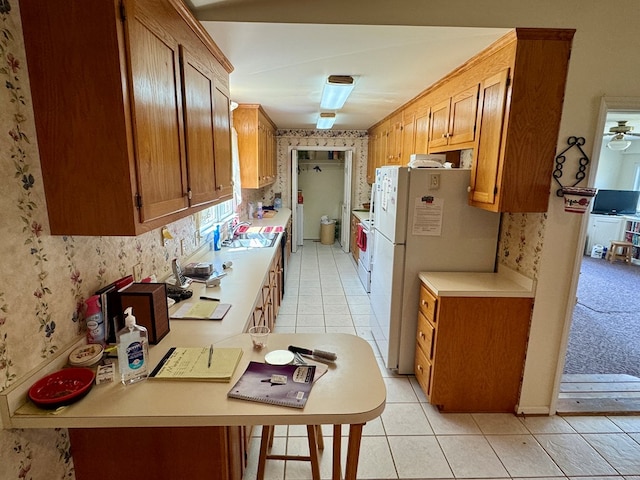 kitchen featuring brown cabinets, a sink, light countertops, wallpapered walls, and light tile patterned floors