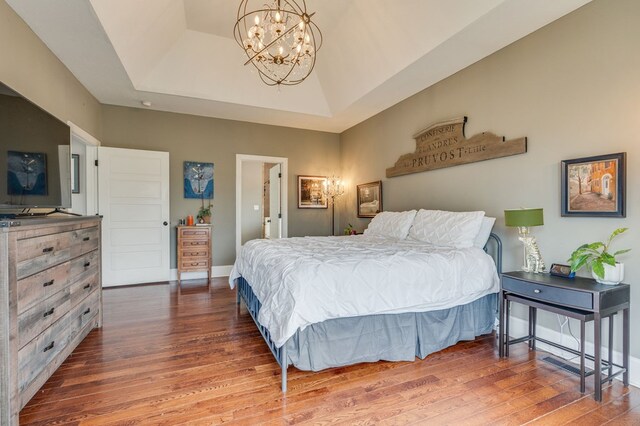 bedroom featuring a notable chandelier, a tray ceiling, baseboards, and wood finished floors