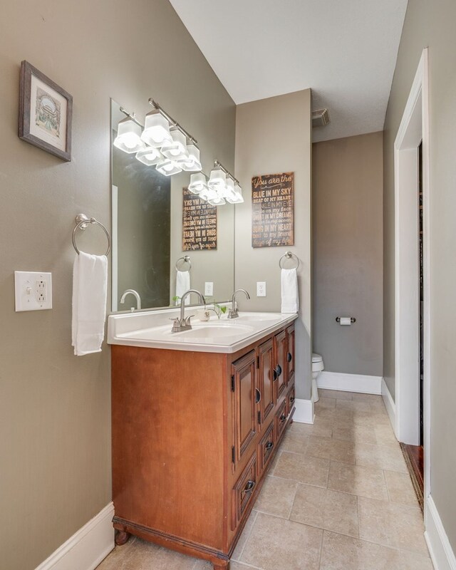 full bath featuring a sink, visible vents, baseboards, and double vanity