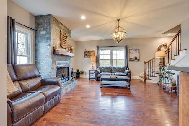 living room featuring an inviting chandelier, wood finished floors, stairway, and a fireplace