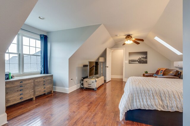 bedroom featuring lofted ceiling with skylight, baseboards, wood-type flooring, and ceiling fan