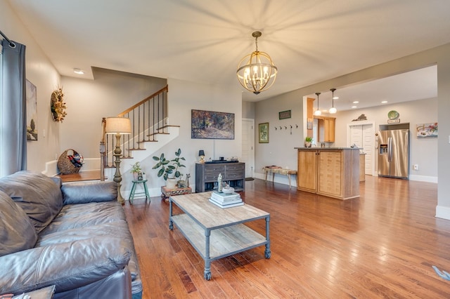 living area with a chandelier, stairs, baseboards, and hardwood / wood-style flooring