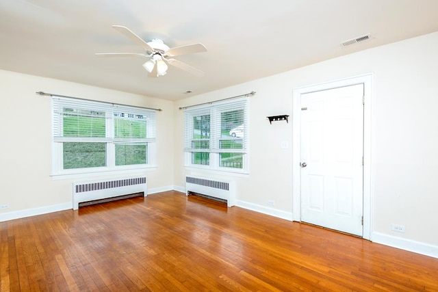 spare room with radiator, a ceiling fan, wood-type flooring, and visible vents