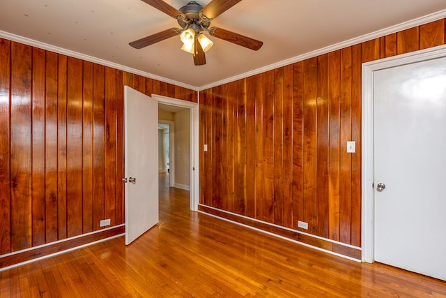 empty room featuring wood finished floors, crown molding, a ceiling fan, and wood walls