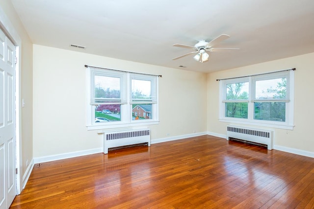 unfurnished room with hardwood / wood-style flooring, visible vents, a ceiling fan, and radiator