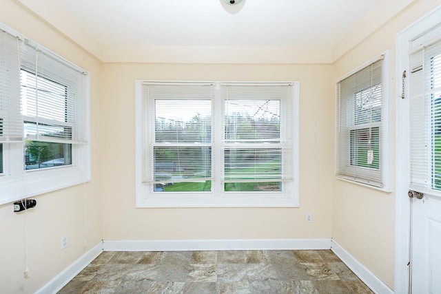 unfurnished room with a healthy amount of sunlight, stone finish flooring, and baseboards