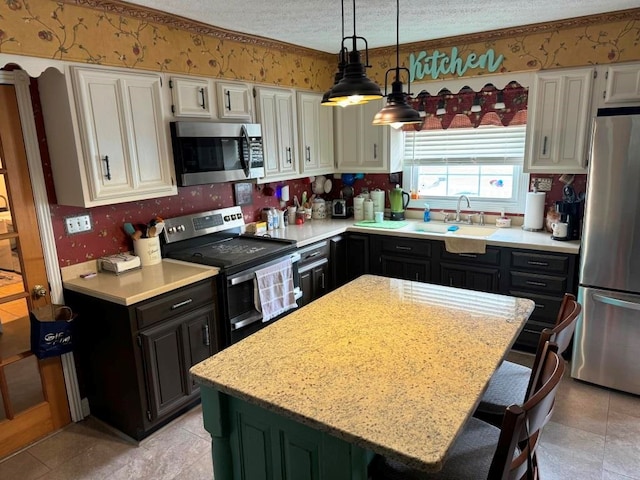 kitchen with wallpapered walls, appliances with stainless steel finishes, white cabinets, a sink, and a textured ceiling