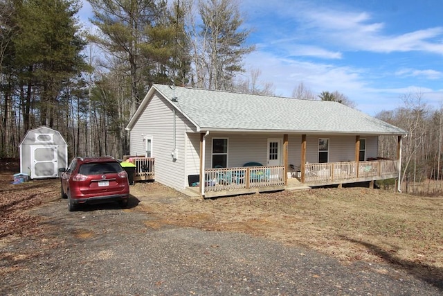 exterior space with an outdoor structure, roof with shingles, a storage shed, and covered porch