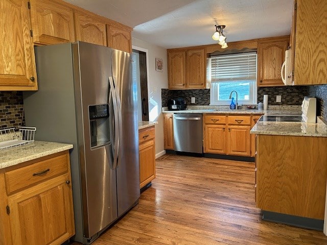 kitchen featuring sink, light wood-type flooring, light stone countertops, and appliances with stainless steel finishes