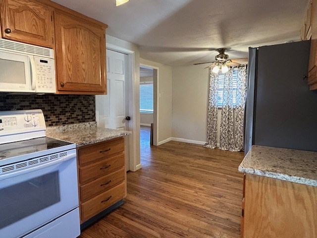 kitchen featuring white appliances, ceiling fan, light stone countertops, dark hardwood / wood-style flooring, and decorative backsplash