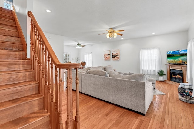 living room featuring light wood-style flooring, a ceiling fan, recessed lighting, stairway, and a lit fireplace