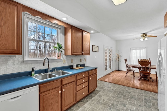 kitchen with a sink, dark countertops, white appliances, brown cabinetry, and decorative backsplash