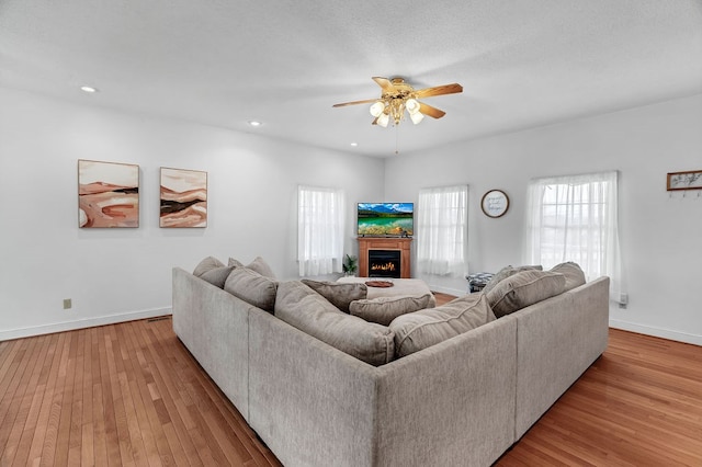 living area featuring hardwood / wood-style flooring, a ceiling fan, baseboards, and a lit fireplace