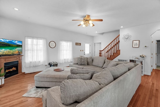 living area featuring visible vents, light wood-style flooring, a warm lit fireplace, recessed lighting, and stairway