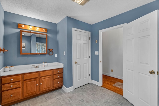 bathroom with baseboards, a textured ceiling, and vanity