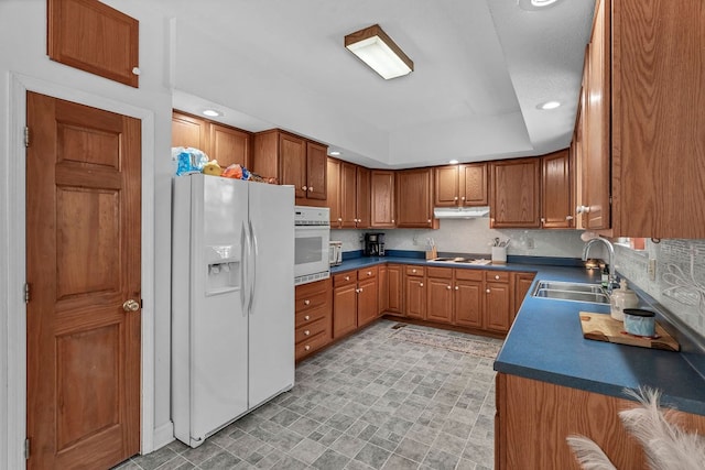 kitchen with white appliances, brown cabinets, under cabinet range hood, and a sink