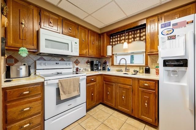 kitchen featuring light countertops, a sink, tasteful backsplash, brown cabinets, and white appliances