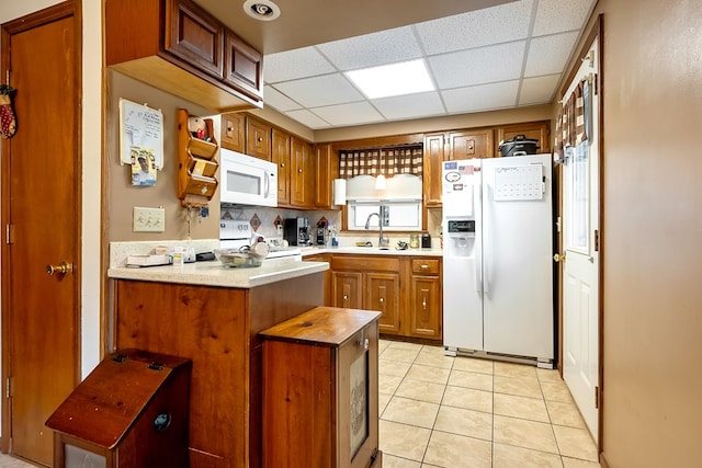 kitchen featuring white appliances, a drop ceiling, light tile patterned flooring, a sink, and brown cabinets