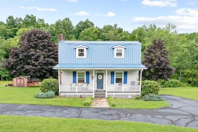 view of front facade featuring a shed, metal roof, a front yard, and covered porch