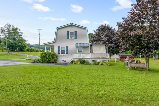 back of property with a gambrel roof, a deck, and a lawn