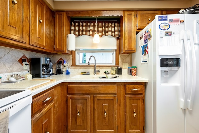 kitchen with brown cabinetry, a sink, white refrigerator with ice dispenser, and light countertops