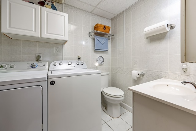 laundry room with light tile patterned flooring, a sink, laundry area, independent washer and dryer, and tile walls