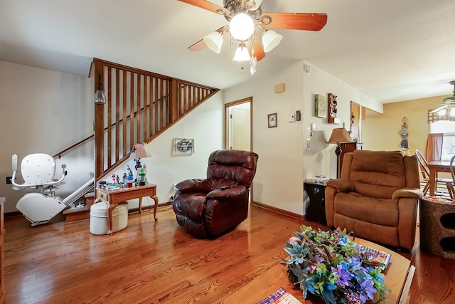 living area with stairs, baseboards, ceiling fan, and wood finished floors