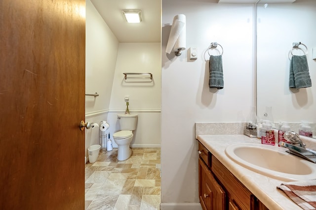 bathroom featuring baseboards, toilet, stone finish flooring, and vanity