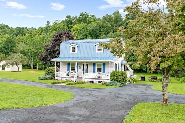 view of front of home with driveway, a front yard, covered porch, a chimney, and metal roof