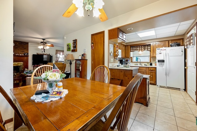 dining space with light tile patterned flooring, a brick fireplace, and a ceiling fan