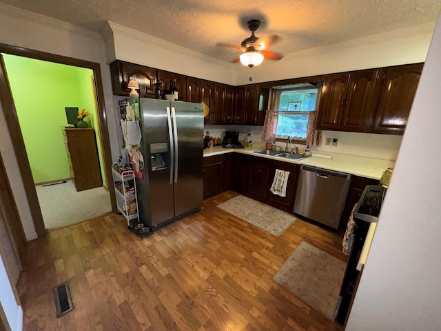 kitchen with light wood finished floors, a sink, stainless steel appliances, light countertops, and dark brown cabinets
