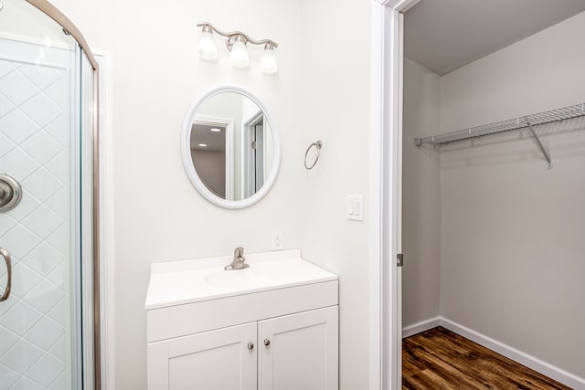 full bath with baseboards, a spacious closet, a shower with door, wood finished floors, and vanity