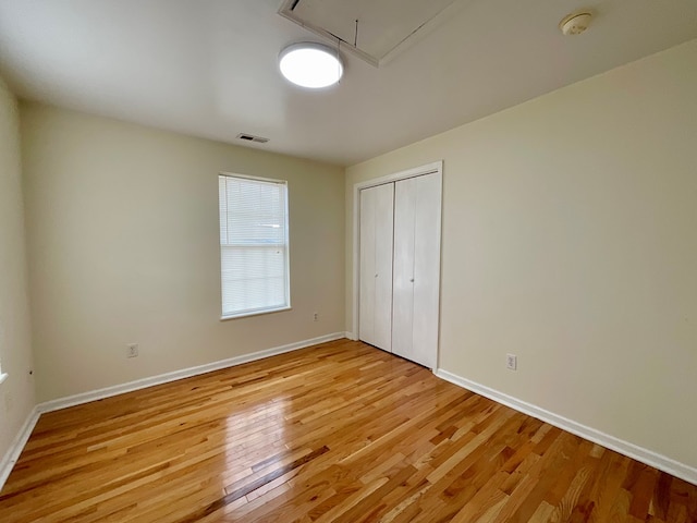 unfurnished bedroom with a closet, attic access, light wood finished floors, baseboards, and visible vents