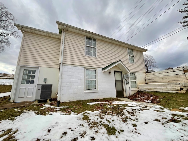 snow covered rear of property featuring central air condition unit and fence