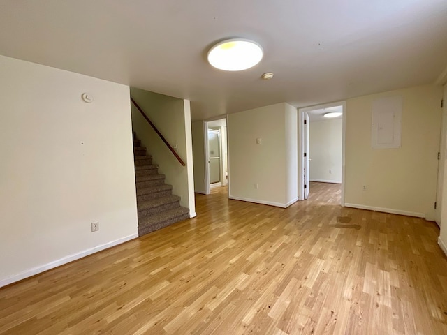 unfurnished living room featuring light wood-style flooring, baseboards, stairs, and electric panel